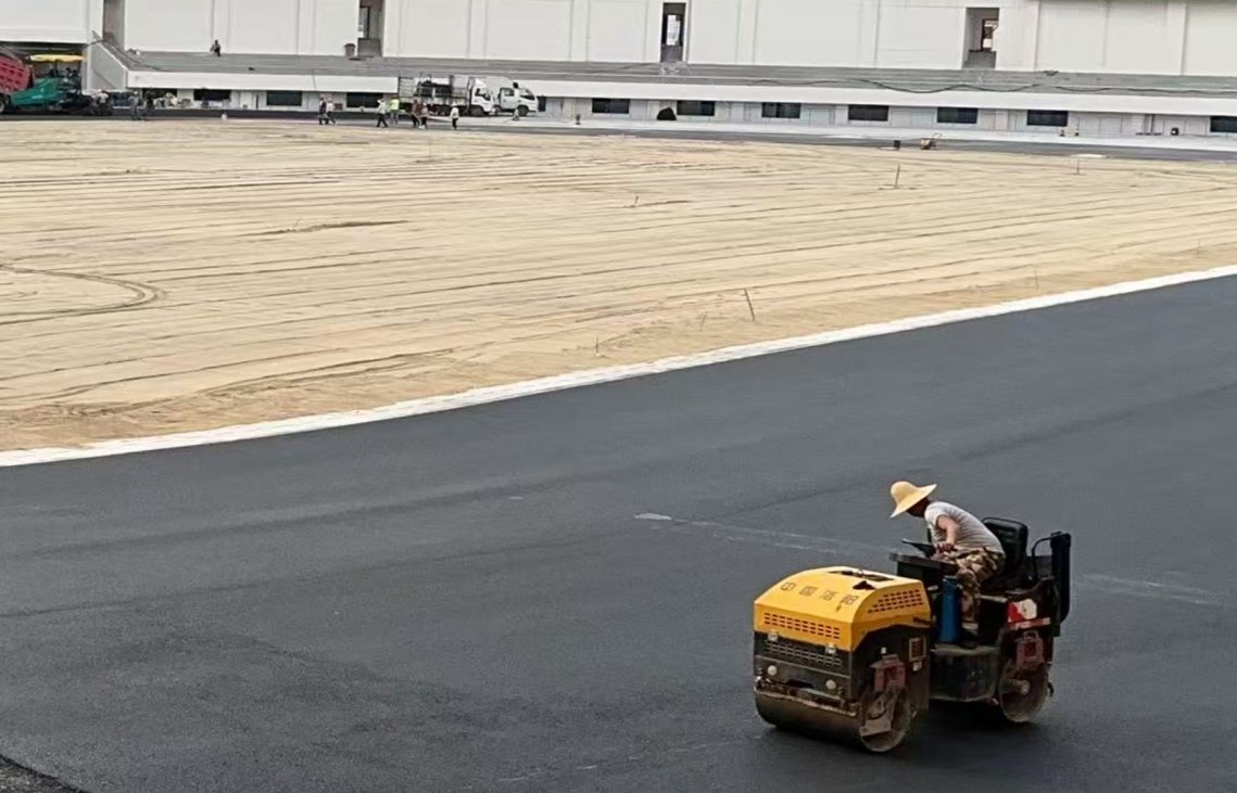 Roller compacting the asphalt foundation of an athletics track